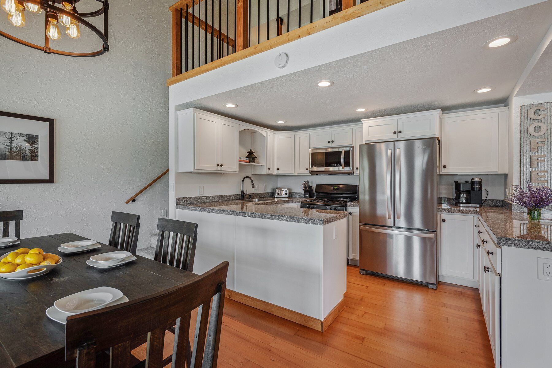 A modern kitchen with white cabinetry, stainless steel appliances, and a wooden dining table with chairs.