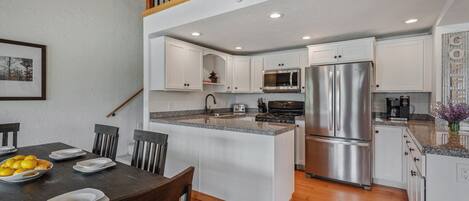 A modern kitchen with white cabinetry, stainless steel appliances, and a wooden dining table with chairs.