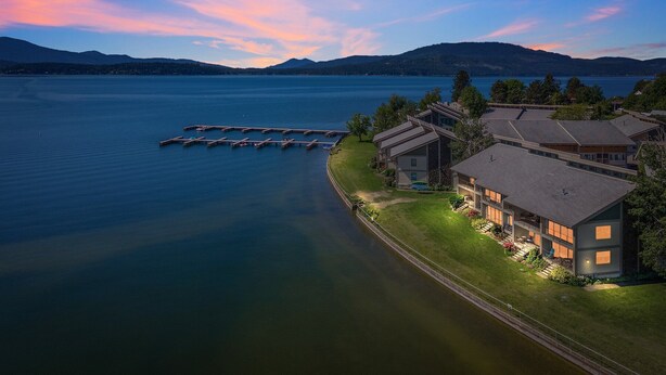 A lakeside property with a dock, modern buildings, and a view of the lake and mountains.