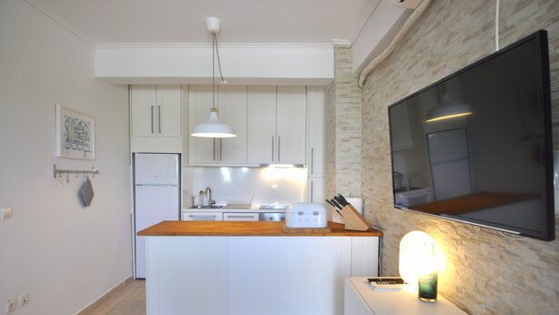 Una cocina moderna con armarios blancos, encimera de madera, horno empotrado y un televisor de pantalla plana grande montado en la pared.