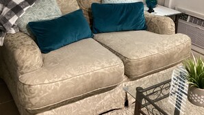 A beige sectional sofa with patterned cushions, a small table with a vase, and a potted plant.