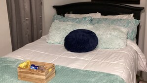 A neatly made bed with a blue pillow, a wooden box on the bed, and a painting on the wall.
