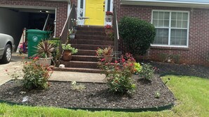 A two-story house with a yellow front door, brick facade, and a small front yard with plants and a driveway.