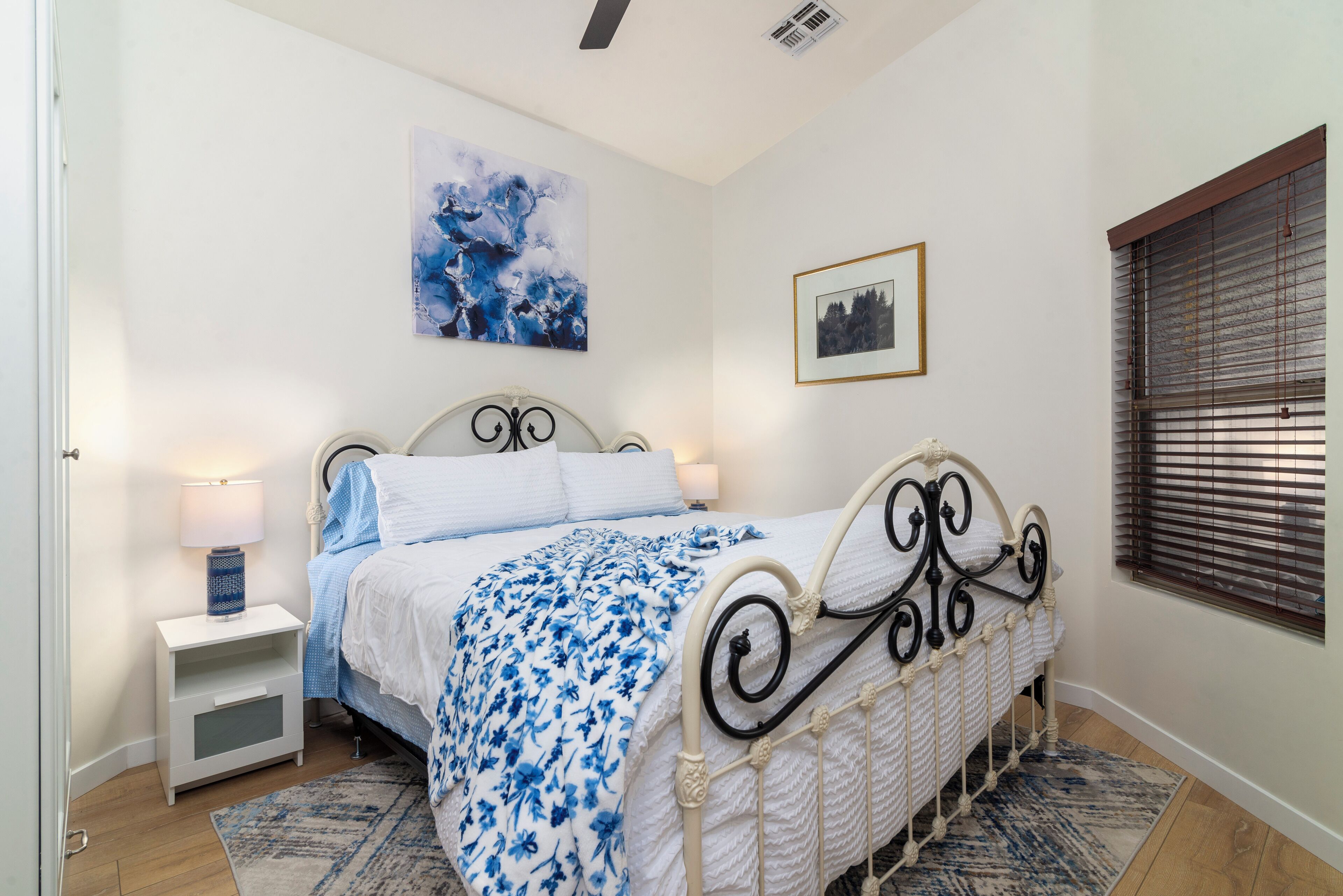 Een slaapkamer met een bed, nachtkastjes, een wanddecoratie en een raam met jaloezieën.