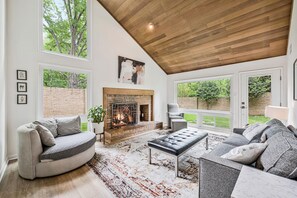 A spacious living room with a fireplace, large windows, and a high ceiling. - Modern Lux Home near DC! (Bethesda)