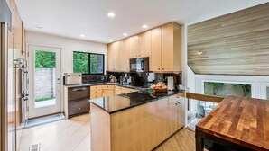 Moderni keittiö, jossa on puiset kaapit, keskellä sijaitseva keittiösaareke ja ruokailutila puupöydän kera.