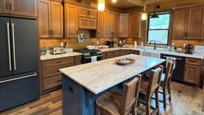 Une cuisine spacieuse avec des meubles en bois, un îlot central doté de chaises et un grand réfrigérateur.