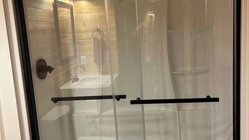 A glass-enclosed shower stall with a black frame, a towel rack, and a mirror on the wall.