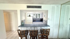 A kitchen with a central island, three wicker chairs, and a view into the dining area.