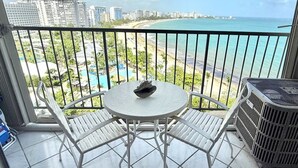 A balcony with a table and chairs, overlooking a beach and cityscape.