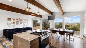 A modern kitchen with a central island, wooden beams, and large windows offering a scenic view. - The Sanctuary at Prescott Heights |Majestic Views |Luxe Prescott Sanctuary |Golf (Prescott)