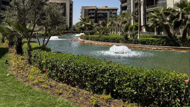 A modern hotel with multiple floors, a landscaped garden, and a water feature.