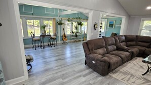 Amplia sala de estar con un sofá modular grande, comedor con mesa y sillas, y vista a un lago a través de amplios ventanales.