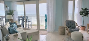 Relax in this inviting living area with a sofa set, wicker chair, and potted plant, leading to a balcony with a water view.