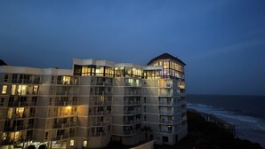 Monikerroksinen hotelli, jossa on parvekkeet ja suuret ikkunat, ja josta avautuu näkymä rannalle ja merelle.
