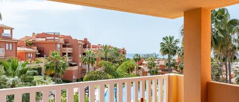 A balcony with a table, a bottle of wine, and a glass, overlooking a pool and palm trees.