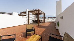 Una terraza en la azotea con una pérgola, asientos al aire libre y vistas al mar.