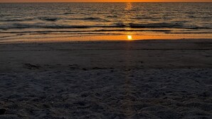 Una playa al atardecer, con el sol ocultándose en el horizonte.