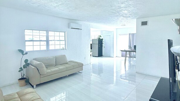 Un salón amplio con un sofá grande, una mesita de centro y un televisor. Hay una planta en maceta y una ventana que proporciona luz natural.
