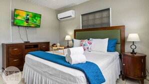 A neatly arranged hotel room with a large bed, two bedside tables, a TV mounted on the wall, and an air conditioning unit. - Cinderella Oasis (Noord)