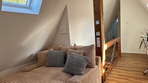 Una camera da letto mansardata con soffitto spiovente, un'ampia finestra, una scala in legno e un letto con testiera.