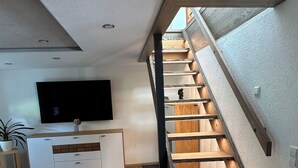 Un soggiorno moderno con una scala in legno, un televisore a schermo piatto e un mobile TV bianco.