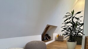 Una stanza con pavimento in legno, due pouf lavorati a maglia, una pianta in vaso e un soffitto spiovente con una piccola finestra.