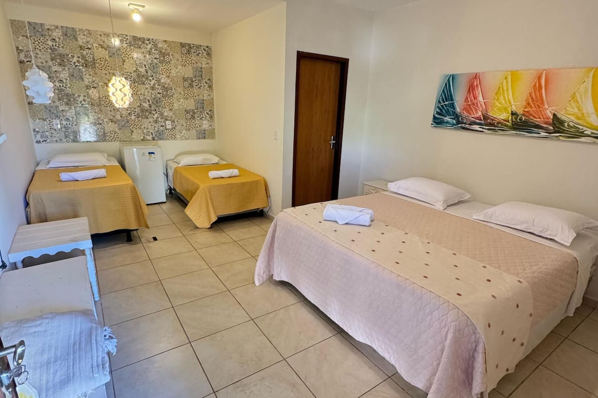 Une chambre d’hôtel avec deux lits simples, un grand lit, un sol carrelé, un mur orné d’un motif décoratif, un luminaire au plafond, une porte et un tableau.