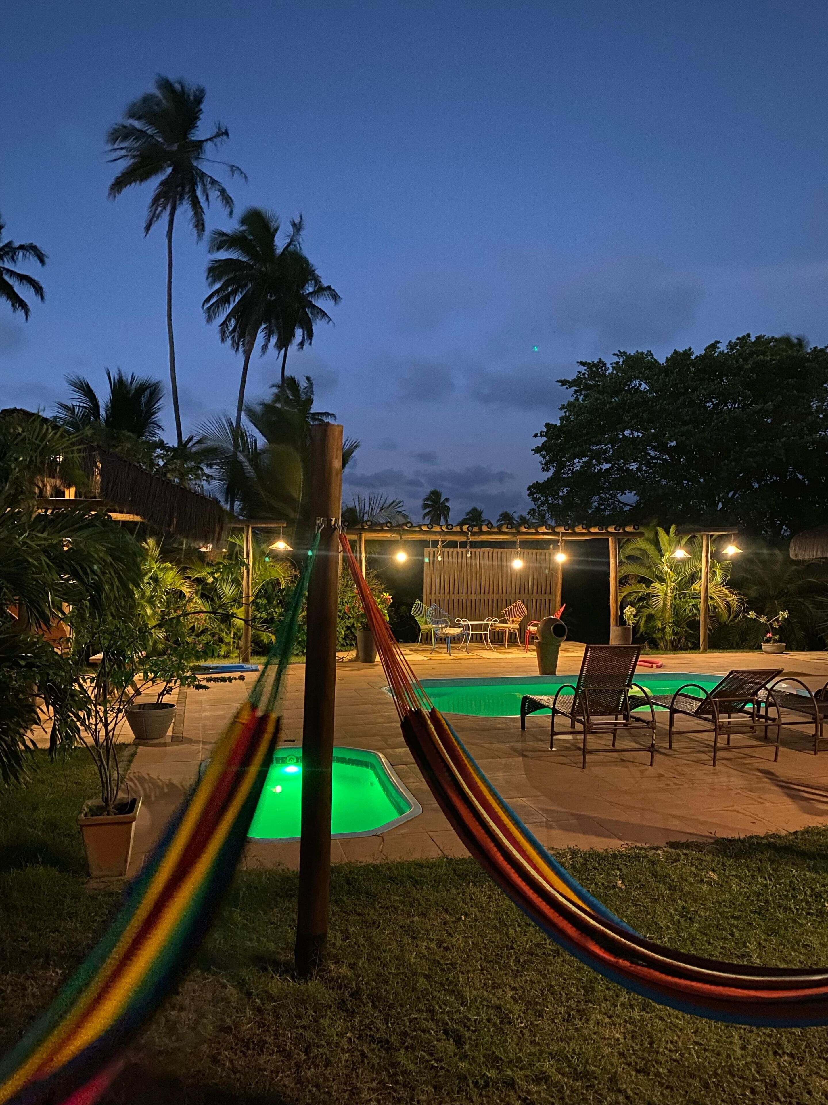 A nighttime outdoor pool area with lounge chairs and a hammock.