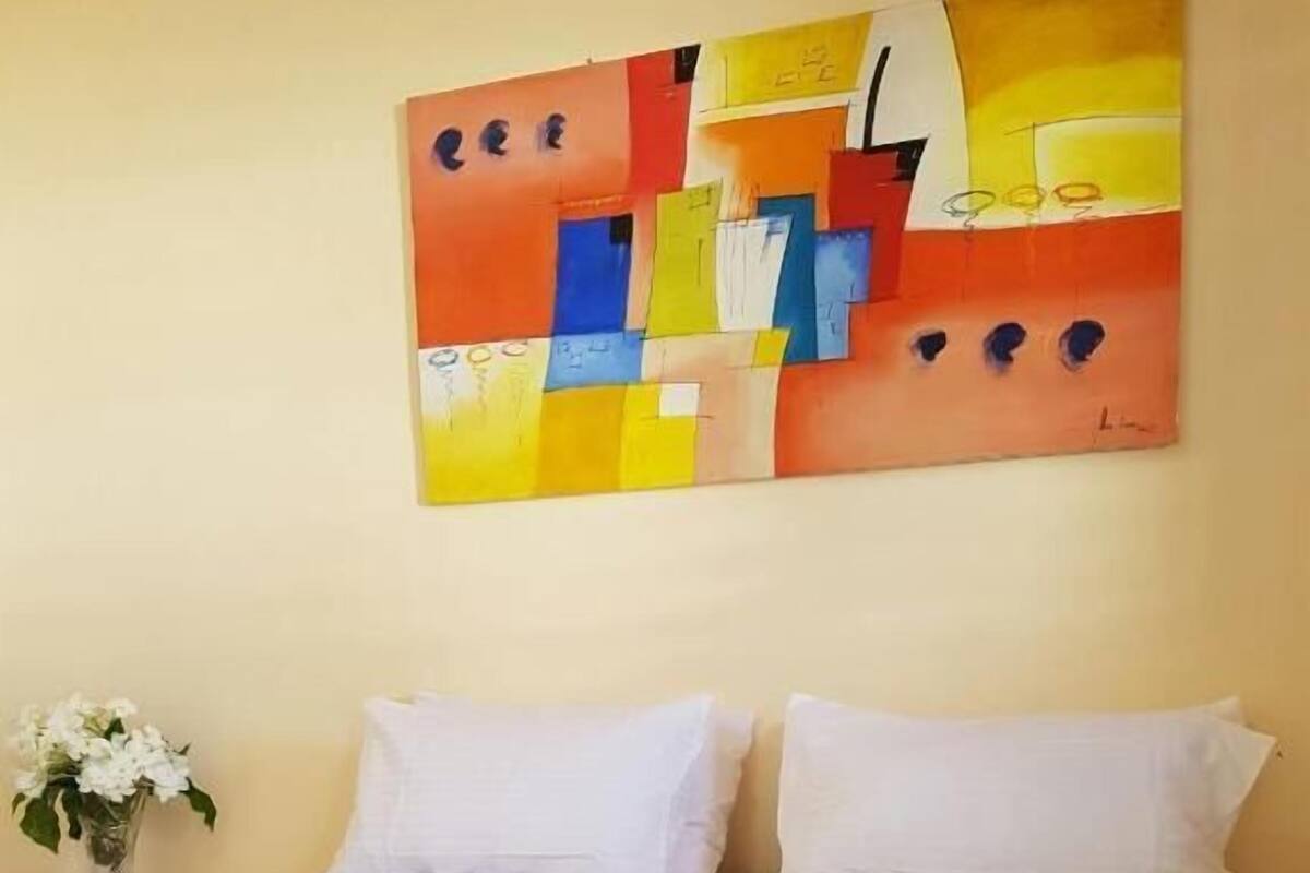 Une chambre d’hôtel avec un grand lit, des oreillers blancs et un tableau abstrait aux couleurs vives accroché au mur.