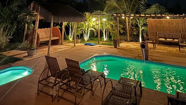 A nighttime pool area with lounge chairs and a thatched-roof structure.
