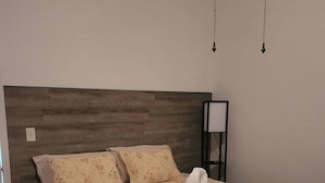 Una cama bien hecha con ropa de cama floral y una toalla blanca encima, un cabecero de madera y una mesita de noche con una lámpara.