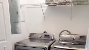 Un cuarto de lavandería con dos lavadoras y secadoras de acero inoxidable, una puerta blanca y piso de madera.