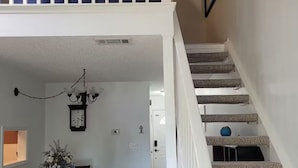 Amplia sala de estar con una mesa de comedor, sillas, una araña y una escalera que incluye un rascador para gatos.