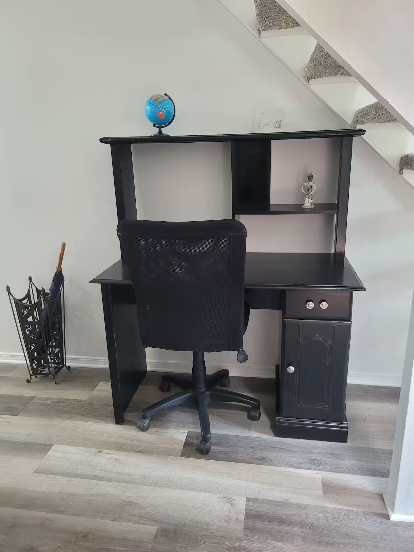 A black office desk with a chair, a globe, and a small statue on the shelf.