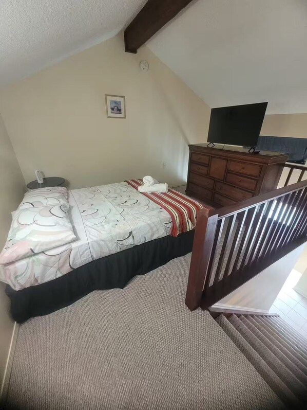 A bedroom with a bed, a dresser, a television, and a picture on the wall.
