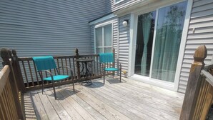A wooden deck with a table and chairs, a sliding glass door, and a view of the house.