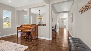 A spacious living room with hardwood floors, a grand piano, a bench, and a large rug.