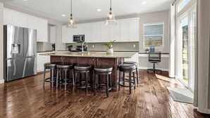A modern kitchen with a central island, bar stools, stainless steel appliances, and pendant lighting.