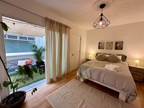Et soveværelse med seng, sengeborde, en hængende lampe, et vindue med gardiner og udsigt til en udendørs patio.