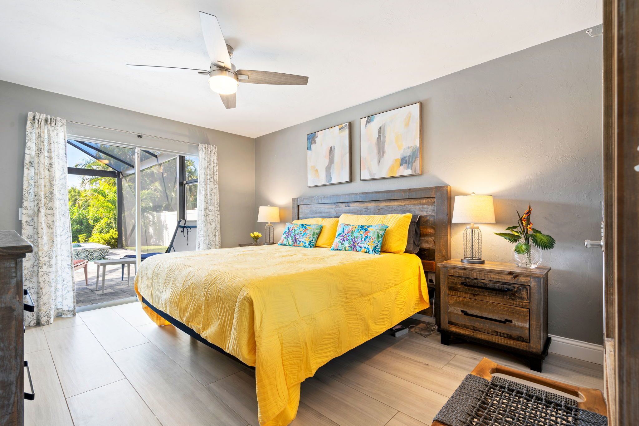 A bedroom with a bed, a ceiling fan, a nightstand, and a view of the outdoors.