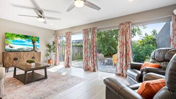 A spacious living room with a large window, ceiling fan, and a view of the backyard.