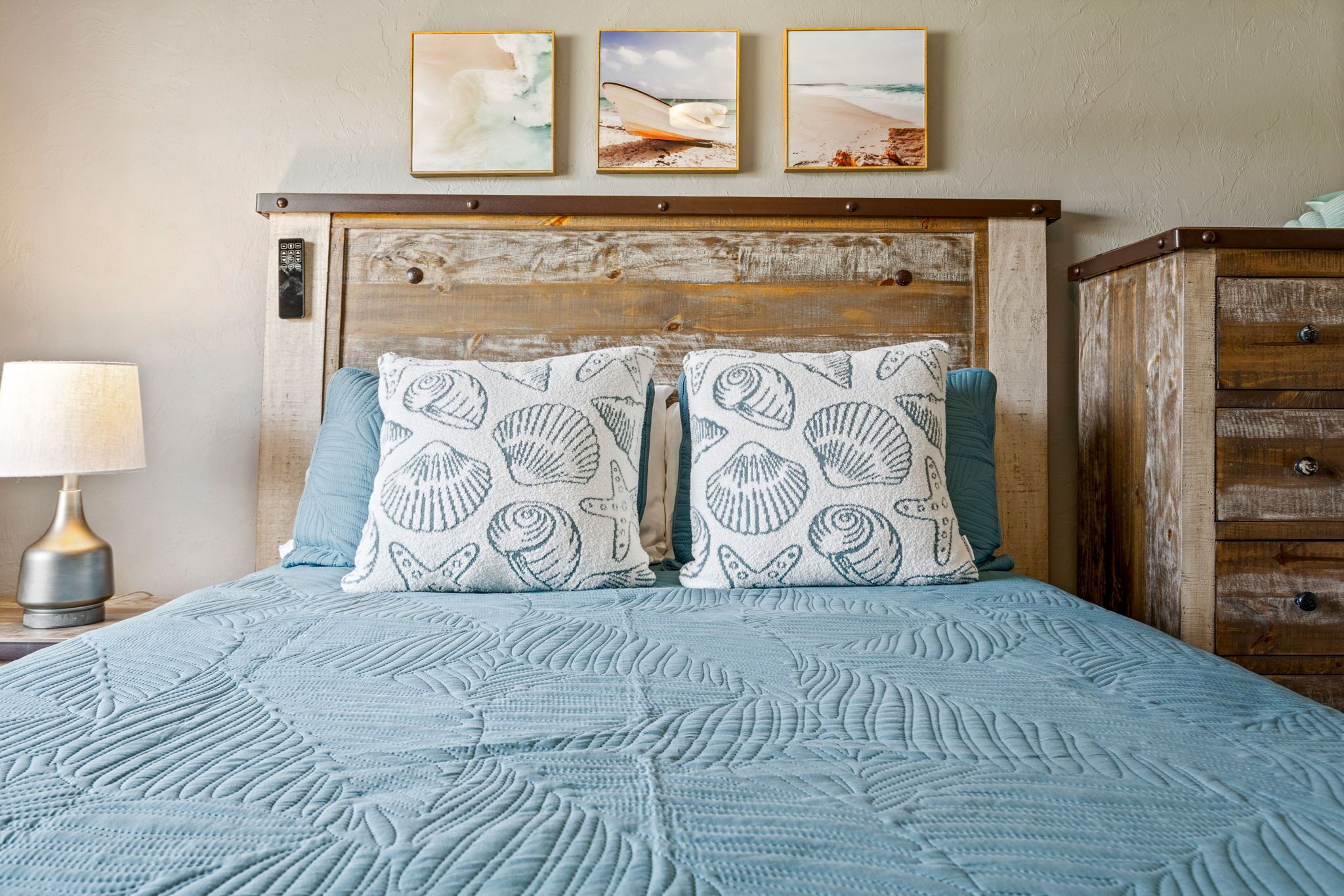 A bed with a blue quilt, two pillows with shell patterns, and a wooden headboard.