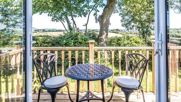 A deck with two chairs and a table, overlooking a tree and a wooden fence.