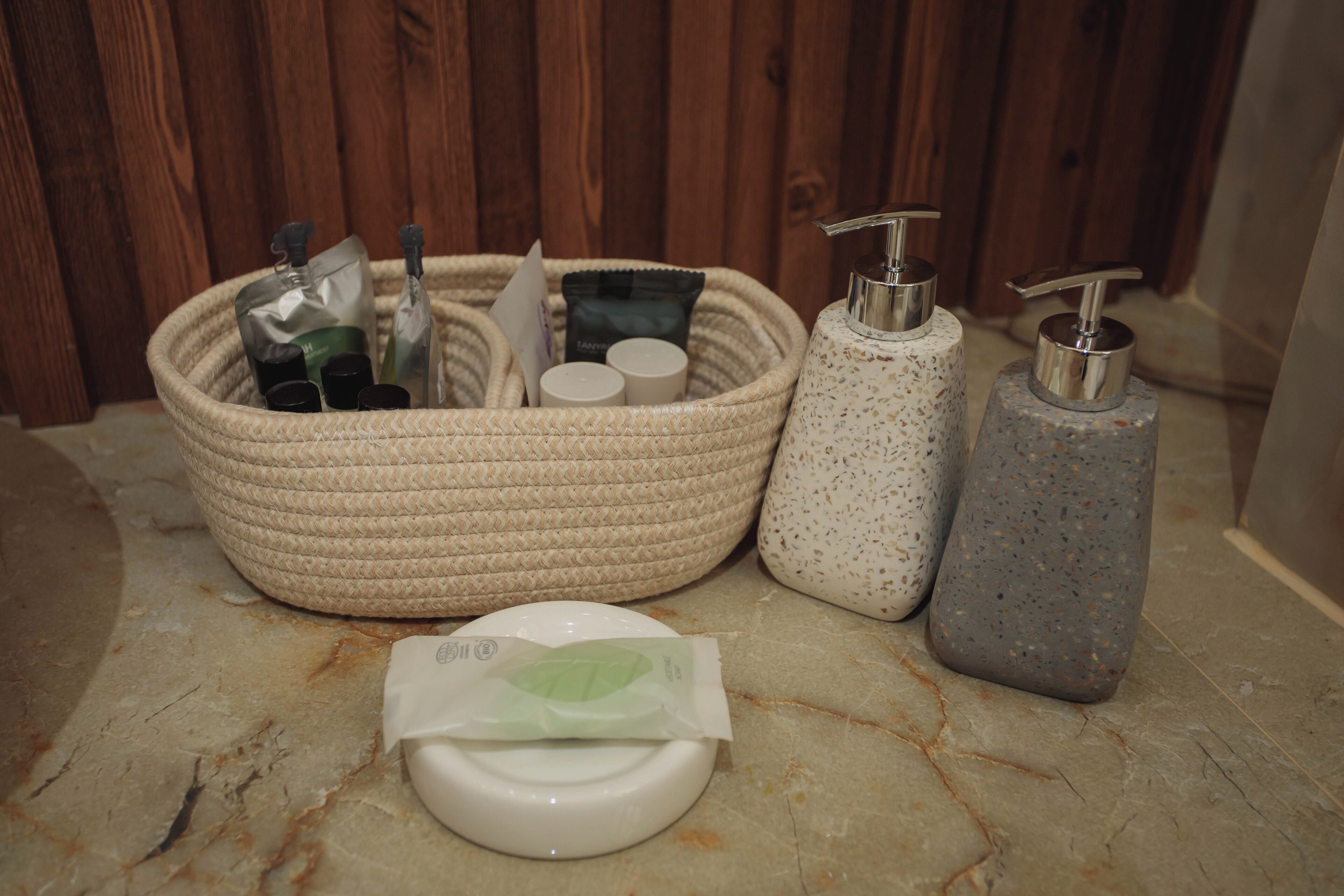 Un bagno con un cesto di vimini contenente articoli da toilette, un dispenser per sapone e un porta carta igienica.