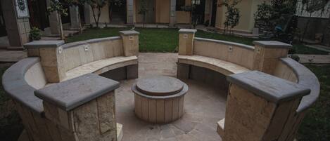 A courtyard with a circular stone seating area surrounded by stone walls, featuring a central fire pit.