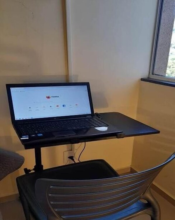 Un ordinateur portable est posé sur une petite table dans une pièce avec une fenêtre.