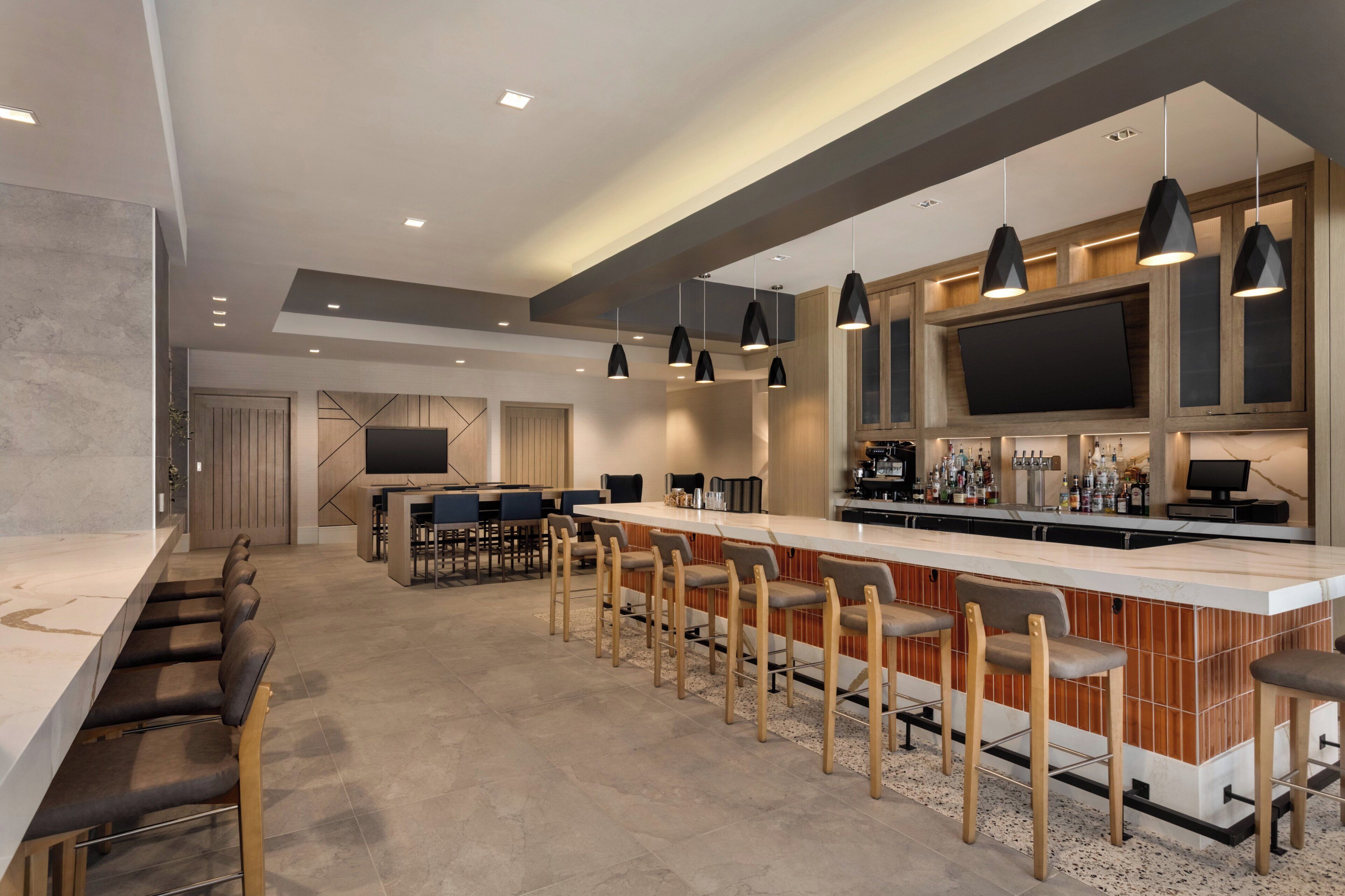 A modern kitchen with a bar area, bar stools, and a large flat-screen TV.