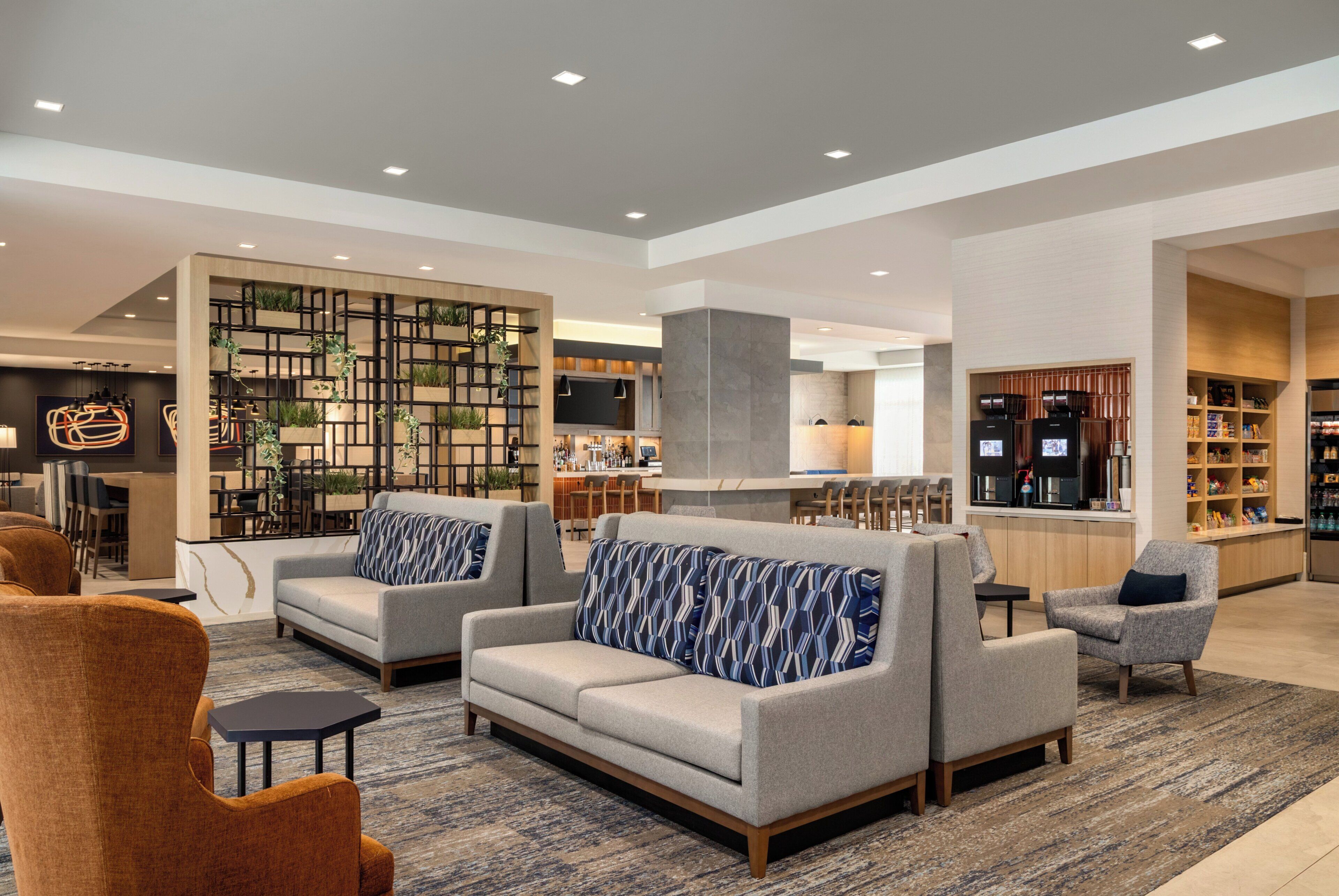 Un vestíbulo moderno con sofás, sillones, una zona de bar y una cocina al fondo.