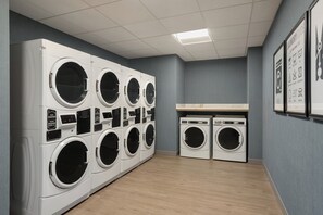 A laundry facility with multiple washing machines and dryers, a tiled ceiling, and a grey wall with a laundry guide. - Holiday Inn Express Houston Downtown by IHG (Houston)
